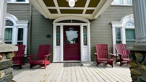 A porch with a red door and stone pillars, surrounded by red Adirondack chairs. - Commanders Cabin, Quaint apt Steps to Downtown (Camden)