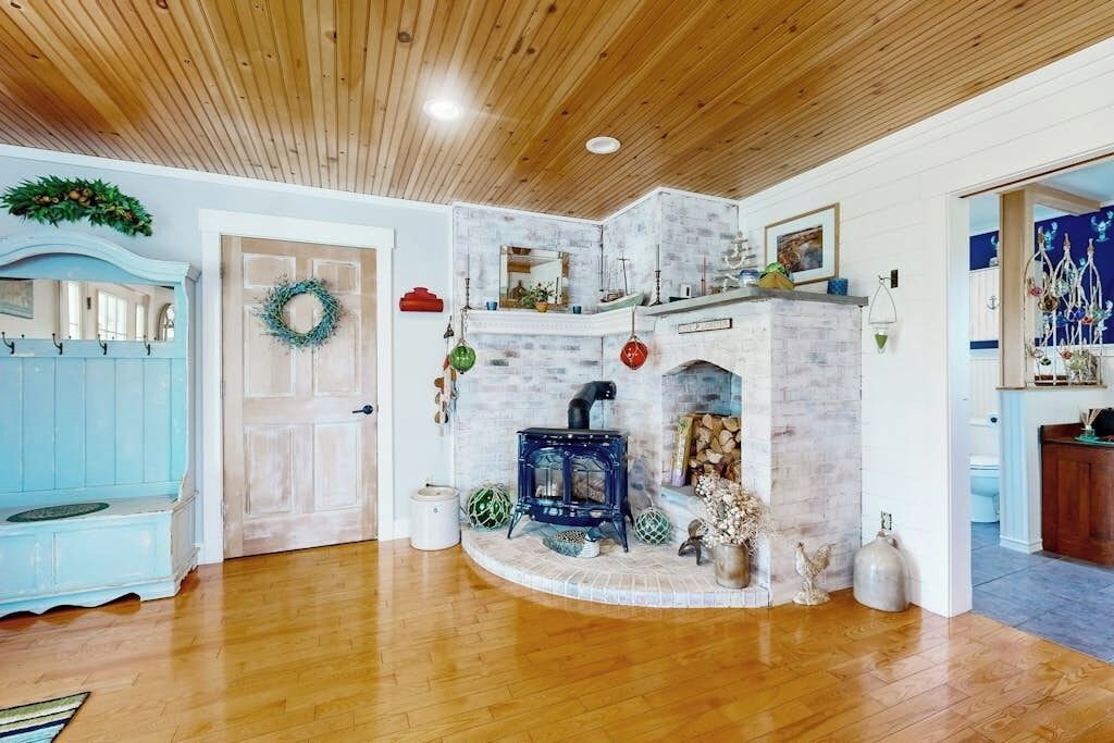 Una habitación con techo de madera, una chimenea con estufa azul, un banco azul y una puerta con un adorno de lazo.