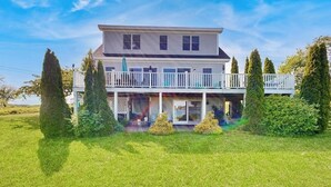Une maison à deux étages dotée d’un balcon, entourée d’une pelouse bien entretenue et de grands arbres.