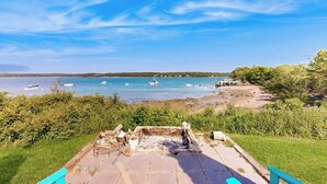 Une plage avec vue sur un foyer, des bateaux sur l’eau et une zone herbeuse.