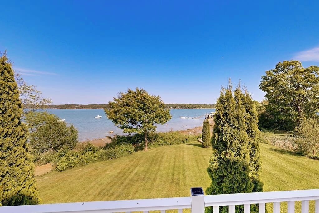 A view from a balcony overlooking a well-maintained lawn, a body of water, and a distant shoreline.
