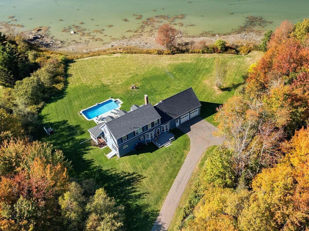 Uma casa grande com piscina, rodeada por um gramado bem cuidado e árvores.