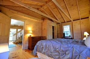 Ein Schlafzimmer in einer Holzhütte mit einem Bett, einem Schminktisch und einer Treppe, die in einen oberen Bereich führt.