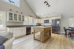 A kitchen with white cabinets, a wooden island, stainless steel appliances, and a dining area with chairs. - Modern Farmhouse With Deck, Firepit, & Balcony (Lincolnville)