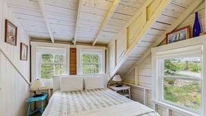Ein Schlafzimmer mit einem Bett, zwei Fenstern, einer Lampe und Blick auf Grünflächen.