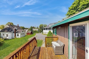 A wooden deck with a wicker sofa, a glass door, and a view of neighboring houses. - Beautifully Updated Cabin Near Town & Barrett (Boothbay Harbor)