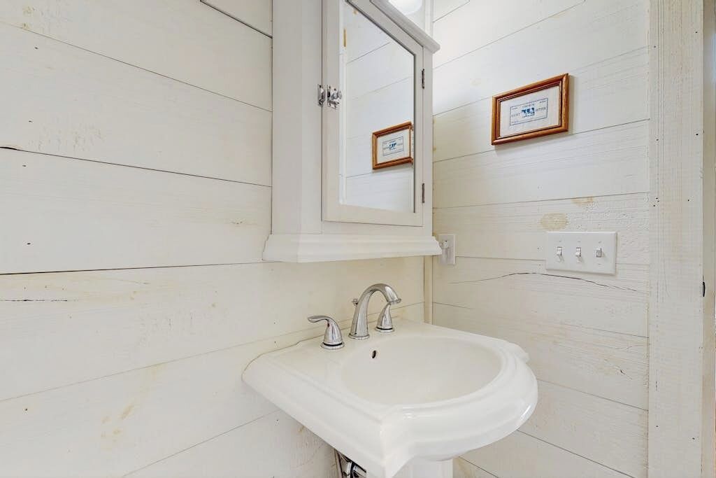 Une salle de bain avec un lavabo blanc, un miroir au-dessus, et deux certificats encadrés accrochés au mur.