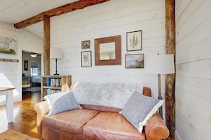 A cozy living room with a brown leather sofa, a wooden beam ceiling, and framed artwork on the wall. - Beautifully Updated Cabin Near Town & Barrett (Boothbay Harbor)