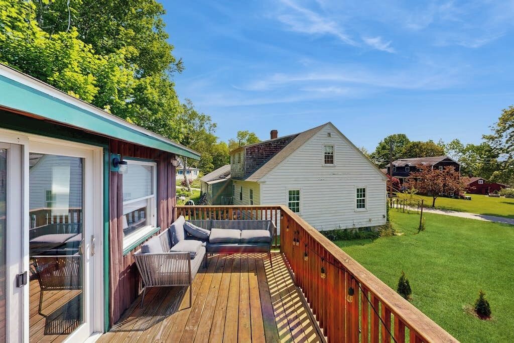 A wooden deck with outdoor furniture, a covered patio, and a white house in the background.