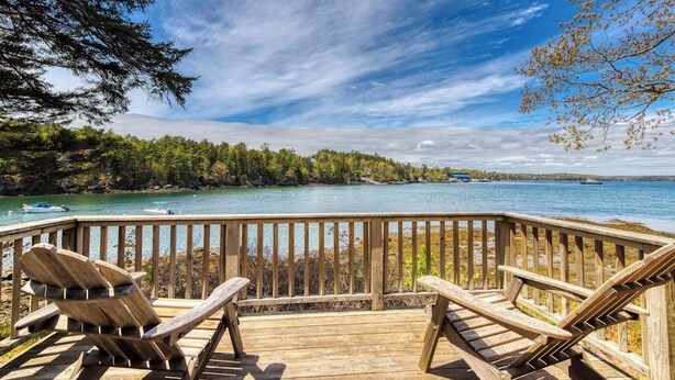 A wooden deck with Adirondack chairs overlooking a lake, surrounded by trees. - Waterfront Cabin With Ocean View & Private Dock (East Boothbay)