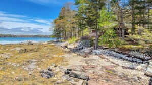 A cabin surrounded by trees and a rocky shoreline. - Waterfront Cabin With Ocean View & Private Dock (East Boothbay)