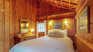 A wooden-paneled bedroom with a bed, bedside lamps, a mirror, and a framed picture on the wall. - Waterfront Cabin With Ocean View & Private Dock (East Boothbay)