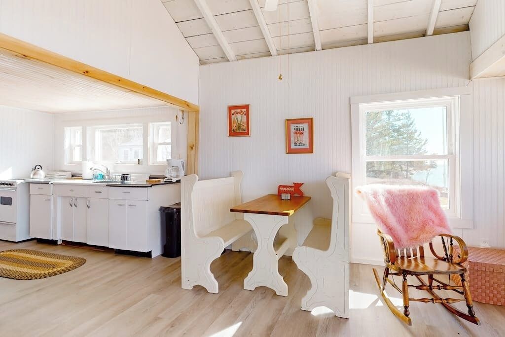 A kitchen with white cabinets, a wooden table, and a rocking chair with a pink blanket.