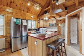 Interior de una cabaña de madera con cocina, un refrigerador, un microondas y una zona de comedor con taburetes.