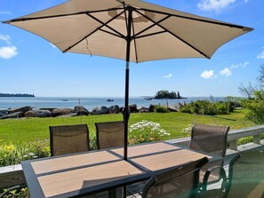 Un patio con mesa y sillas, un gran paraguas y vistas al océano.