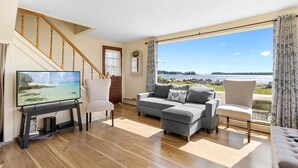 A living room with a television, a sofa, a chair, and a view of a body of water. - Owls Nest on Crescent Beach (Owls Head)