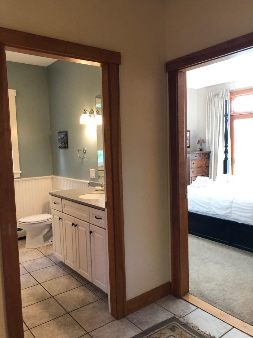 Un baño con inodoro, lavabo y espejo, y un dormitorio con cama y ventana.