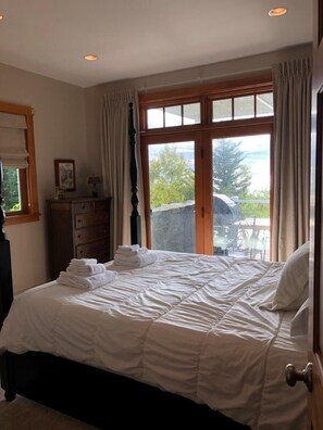 Ein Schlafzimmer mit einem Bett, einem Schminktisch, einem Fenster mit Vorhängen und Blick ins Freie.
