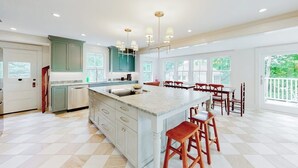 A spacious kitchen with a large island, wooden chairs, and a view of greenery outside. - Beautiful Home With Ping-pong, Fast Wifi & W/D - Walk to Dining (Wiscasset)