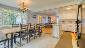 A spacious kitchen with white cabinets, a dining area with a wooden table and chairs, and a chandelier. - Lakefront Cottage w/ Beautiful Views of Moosehead Lake & Big Moose Mountain (Greenville)
