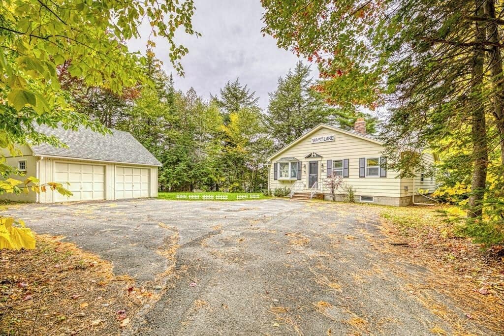 Une maison à deux étages avec un garage, entourée d’arbres et dotée d’une allée.