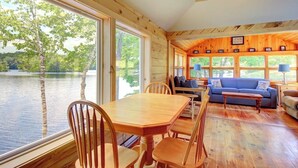 A cabin with a wooden interior, a dining table with chairs, a sofa, and a view of a lake. - Newly Restored Waterfront Cottage With Private Dock, Fireplace, & Farm - Dogs OK (Newcastle)
