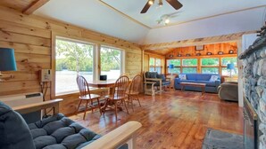A cabin interior with a dining area, seating, a fireplace, and large windows. - Newly Restored Waterfront Cottage With Private Dock, Fireplace, & Farm - Dogs OK (Newcastle)