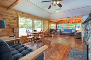A cabin interior with a dining area, seating, a fireplace, and large windows. - Newly Restored Waterfront Cottage With Private Dock, Fireplace, & Farm - Dogs OK (Newcastle)