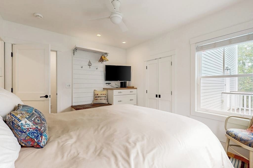A bedroom with a bed, a television, a dresser, and a window.