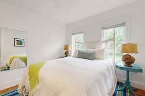 A bedroom with a large bed, two bedside tables with lamps, a mirror, and a window with blinds. - Elegant Home With Veranda & Water View, Walk to Downtown Boothbay Harbor (Boothbay Harbor)