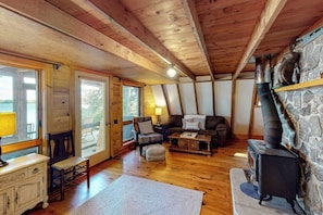 A cozy cabin interior with a stone fireplace, wooden floors, a sofa, a chair, and a table. - Waterfront A-frame on George's Pond With Views, Private Dock, Beach, Kayaks, SUP (Franklin)