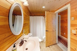 A wooden cabin bathroom with a sink, mirror, and shower curtain. - Waterfront A-frame on George's Pond With Views, Private Dock, Beach, Kayaks, SUP (Franklin)