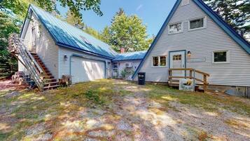 A two-story house with a blue roof, a covered porch, and a gravel driveway.