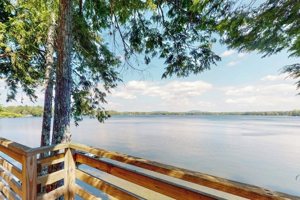 A wooden deck overlooking a calm lake with trees and distant hills.