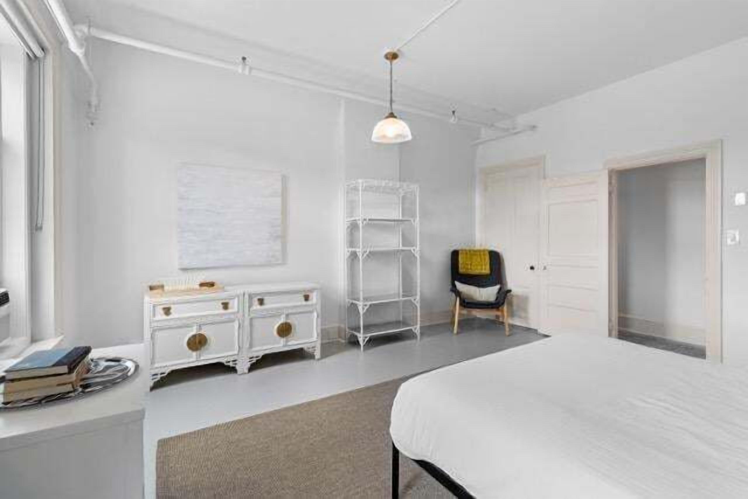 A bedroom with a bed, a white dresser, a chair, a bookshelf, and a door.
