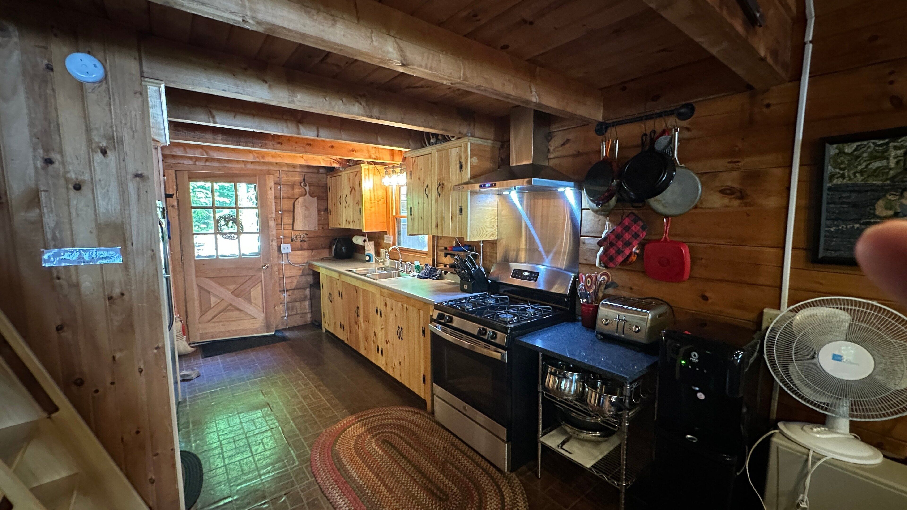 A wooden cabin interior with a kitchen, a stove, a toaster, and a fan.