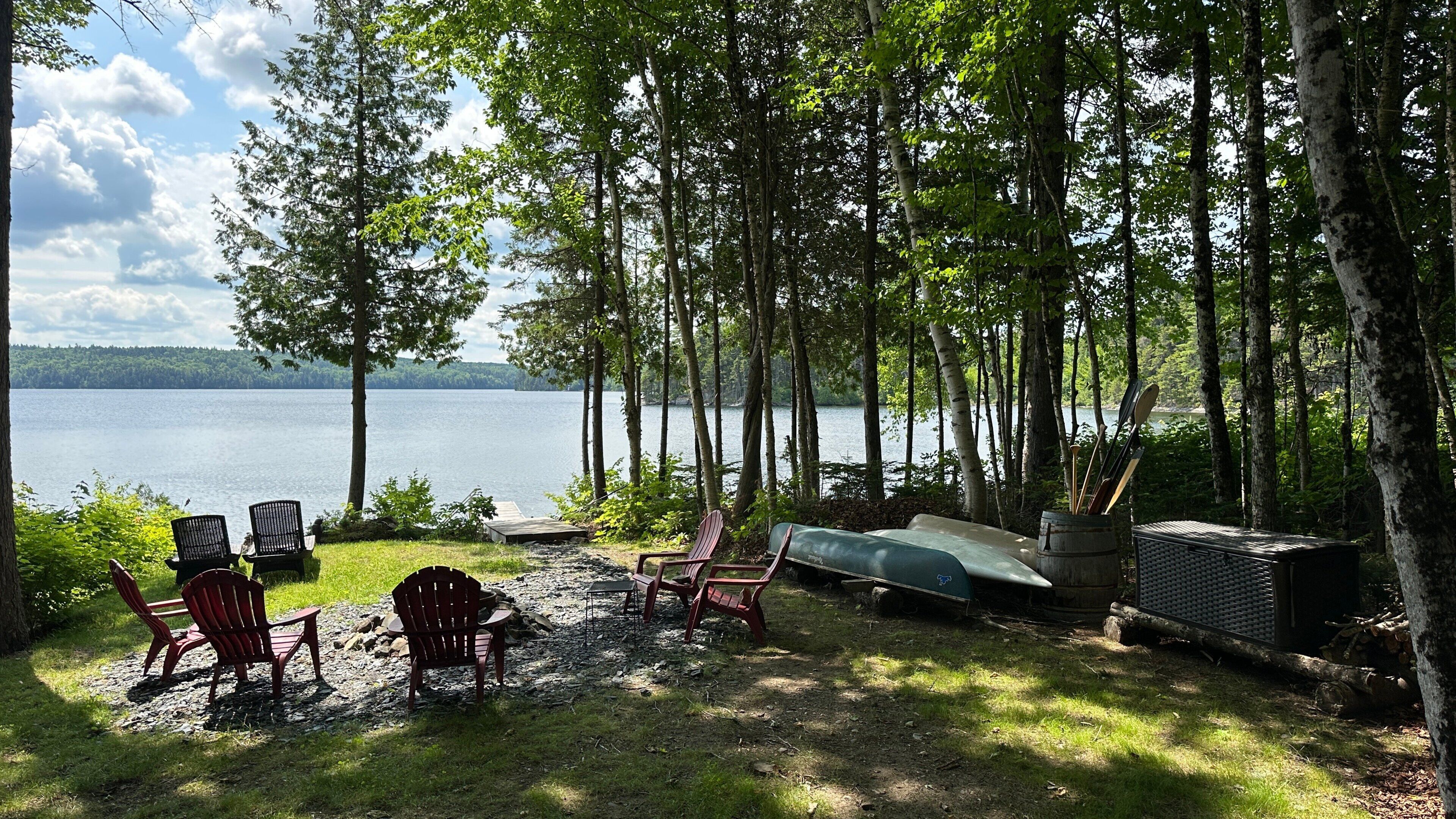 A lakeside deck with chairs, a grill, and a canoe.