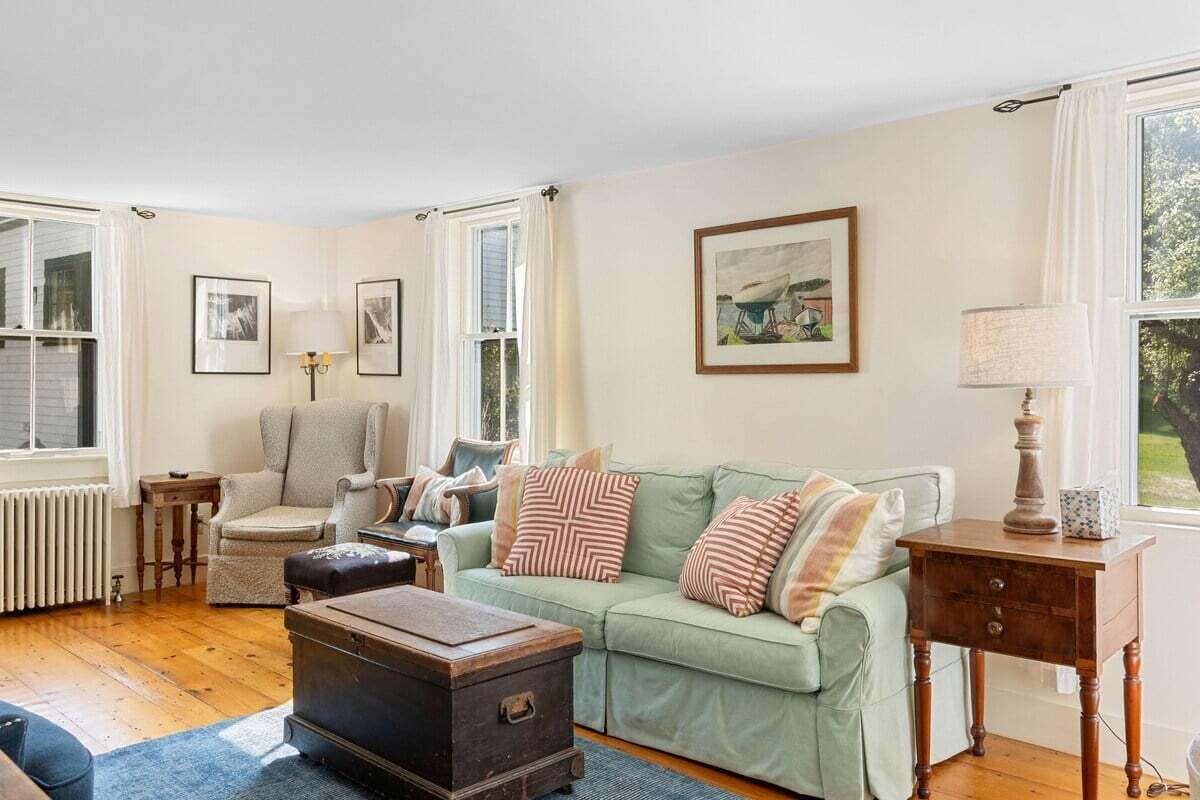A living room with a green sofa, a wooden chest, a chair, and a table with a lamp.