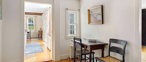 A room with a wooden floor, a dining table with chairs, a radiator, and a window.
