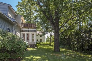 Ein zweistöckiges Haus mit Balkon, umgeben von üppigem Grün und einem großen Baum.