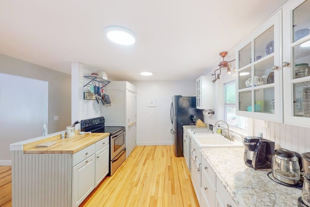 A compact kitchen with white cabinetry, a wooden floor, and a built-in oven.