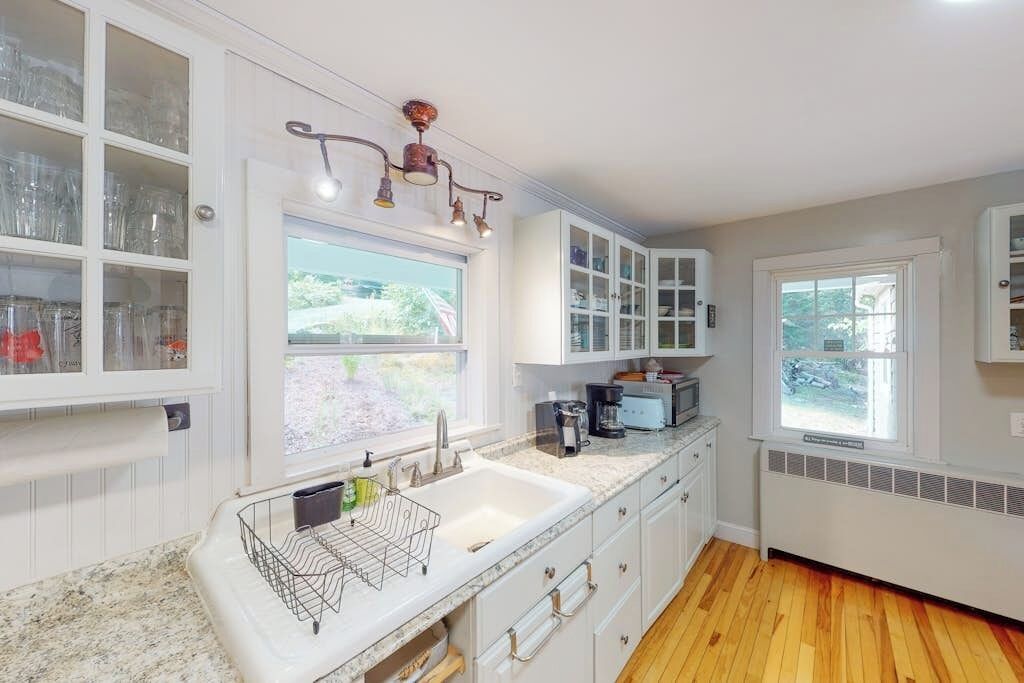 A kitchen with a granite countertop, white cabinets, a built-in sink, and a window with a view of greenery.