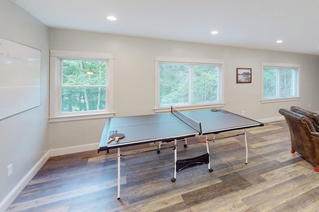 A room with a ping pong table, windows, and a whiteboard.