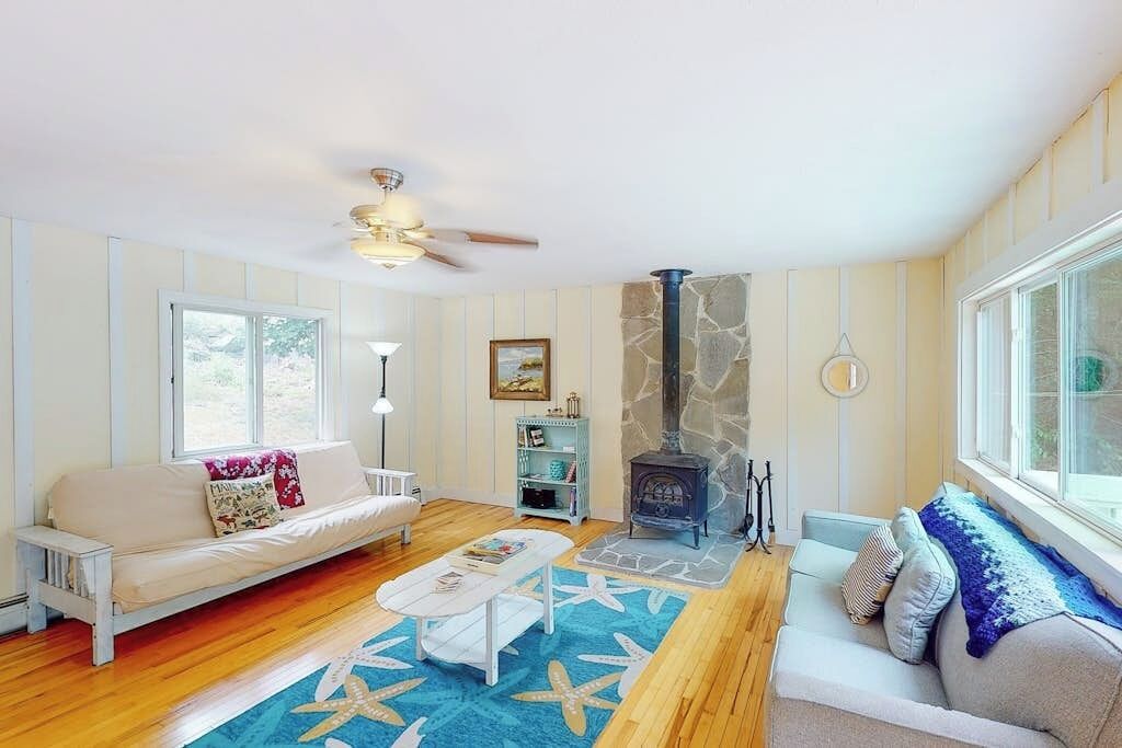 Un salon chaleureux avec une cheminée en pierre, un plancher en bois, un canapé blanc et un tapis bleu.