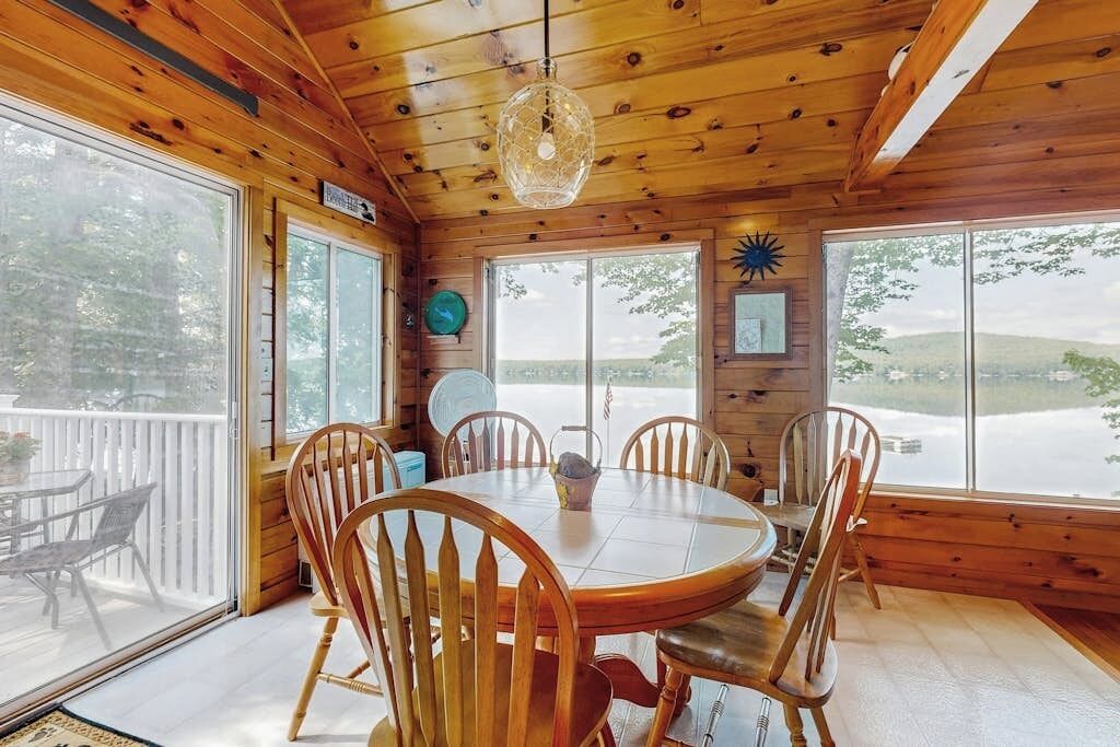 L’intérieur d’un chalet en bois, avec une table à manger ronde, six chaises, de grandes fenêtres et une vue sur un paysage enneigé.
