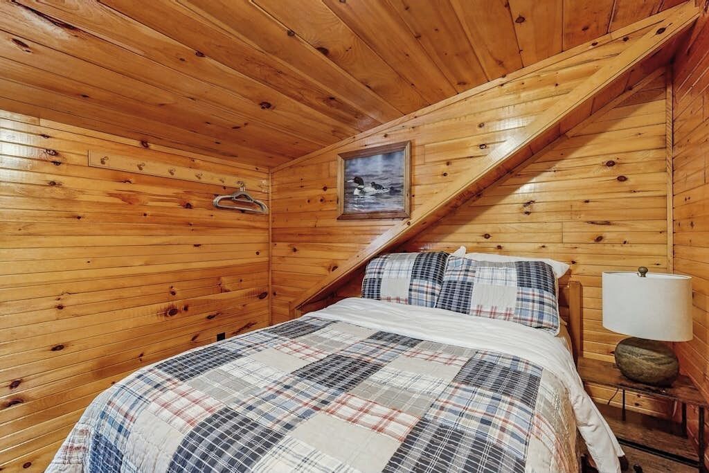 Ein Zimmer in einer Holzhütte mit einem Bett, einer Lampe und einem gerahmten Bild an der Wand.