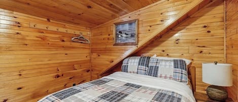 Ein Zimmer in einer Holzhütte mit einem Bett, einer Lampe und einem gerahmten Bild an der Wand.