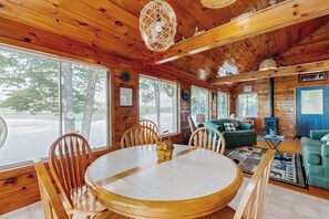 Interior de una cabaña de madera con una mesa de comedor, sillas, un sofá y una chimenea.