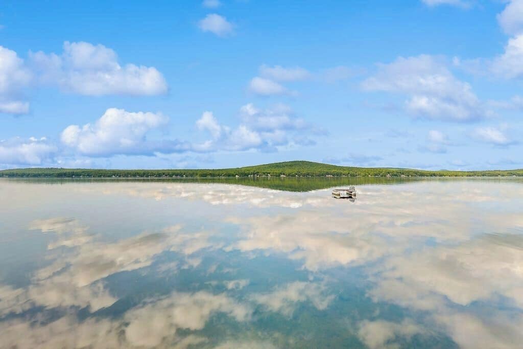 A calm lake with a boat, clear sky, and distant green hills.