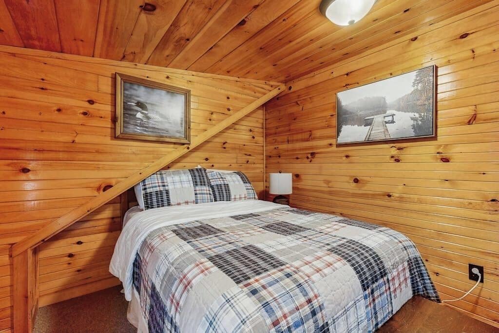 A wooden cabin bedroom with a bed, two framed pictures, and a nightstand.